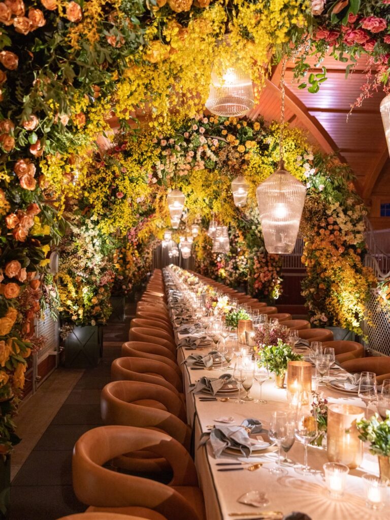 Intimate wedding dinner reception design with lush overhead greenery, warm lighting and candlelit tablescape event designer HMR Designs