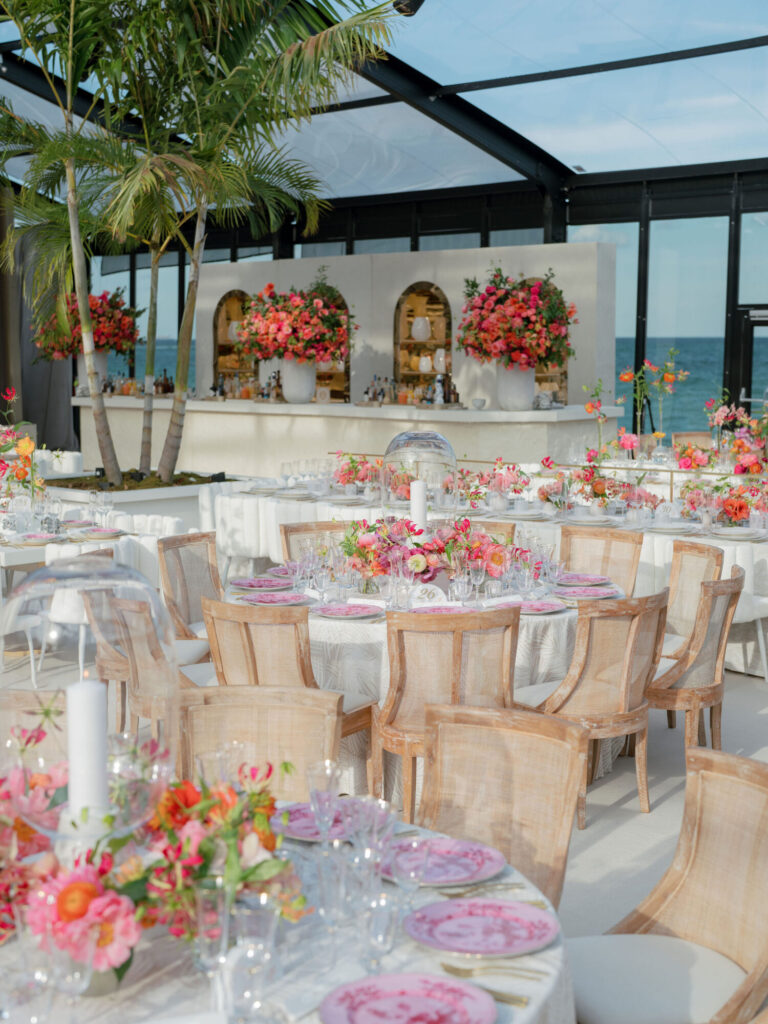 Waterfront wedding reception design with bright pink floral centerpieces and glass walls planning Rishi the Designer