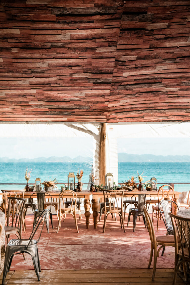 Open-air waterfront wedding reception design with wood ceiling, dining tables and lake views wedding decor Rishi Patel