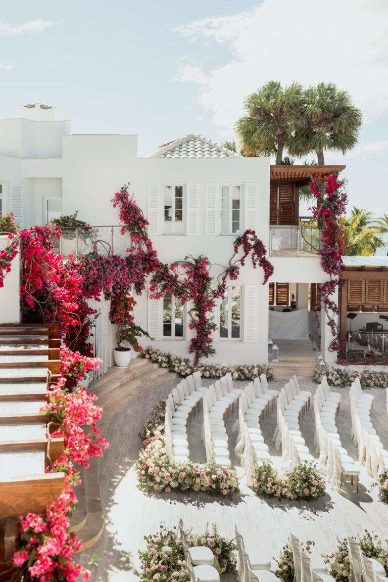 Outdoor wedding ceremony design with vivid pink floral installations and white seating by Rishi Patel