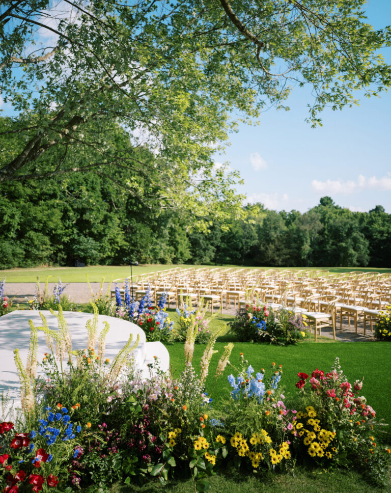 Outdoor destination wedding ceremony design with rows of chairs and colorful floral arrangements event designer HMR Designs