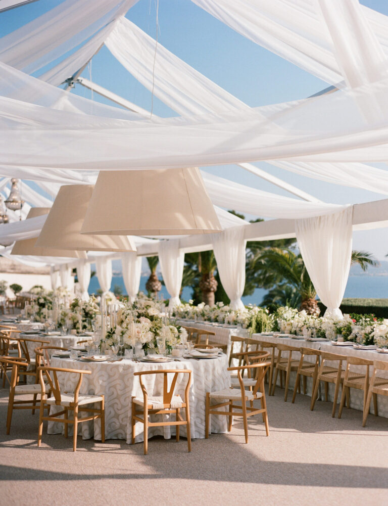 Tented wedding design reception with white draping, wooden chairs and neutral floral arrangements designer Rishi Patel