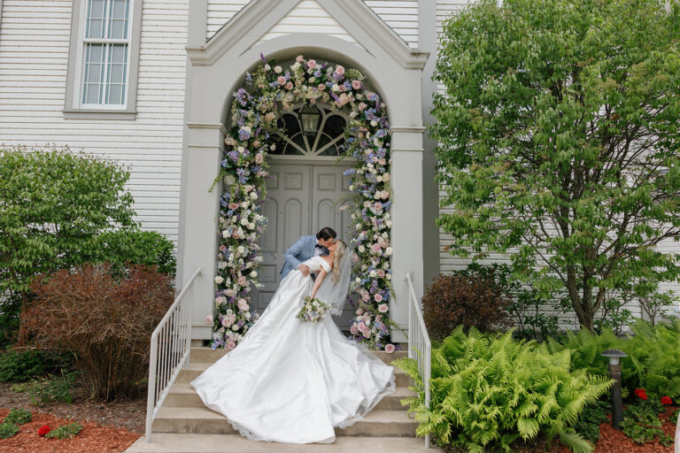 Bride beneath a floral-covered archway outside a white church wedding design by Rishi the Designer