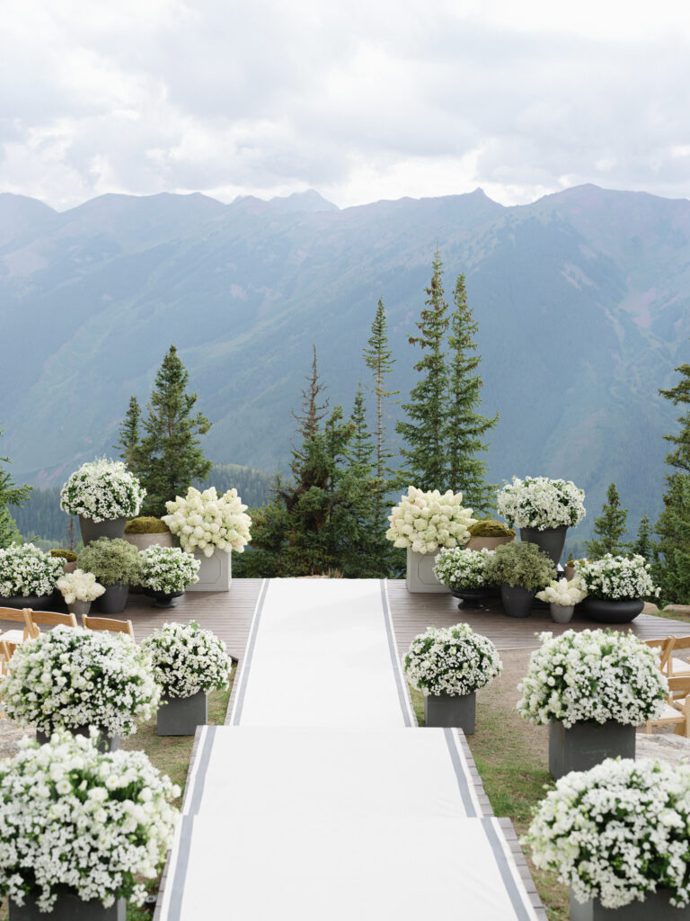 A white aisle cascades down a series of steps to a ceremony framed by mountains and lush florals.