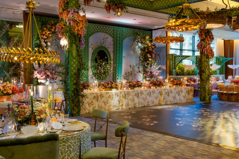 Luxury wedding reception with green trellis walls, cascading wisteria and floral columns, floral print head table linen, and gold chandeliers