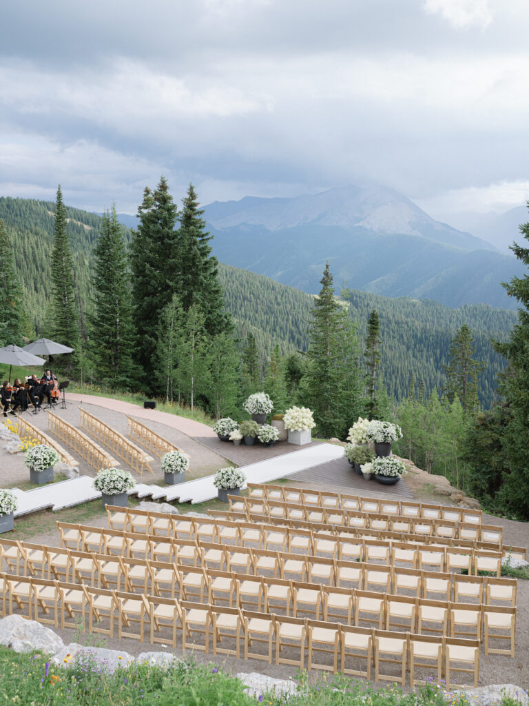 A white aisle cascades down a series of steps to a ceremony framed by mountains and lush florals.