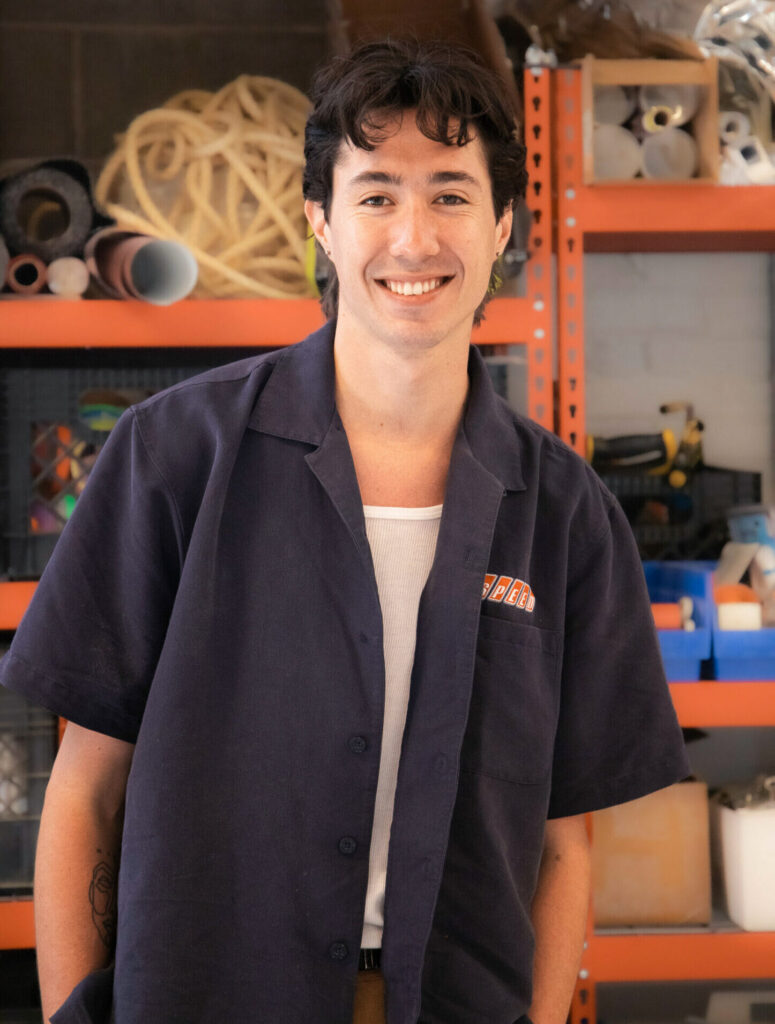 Devin Walls, Scenic Designer at HMR Designs, smiling in the workshop