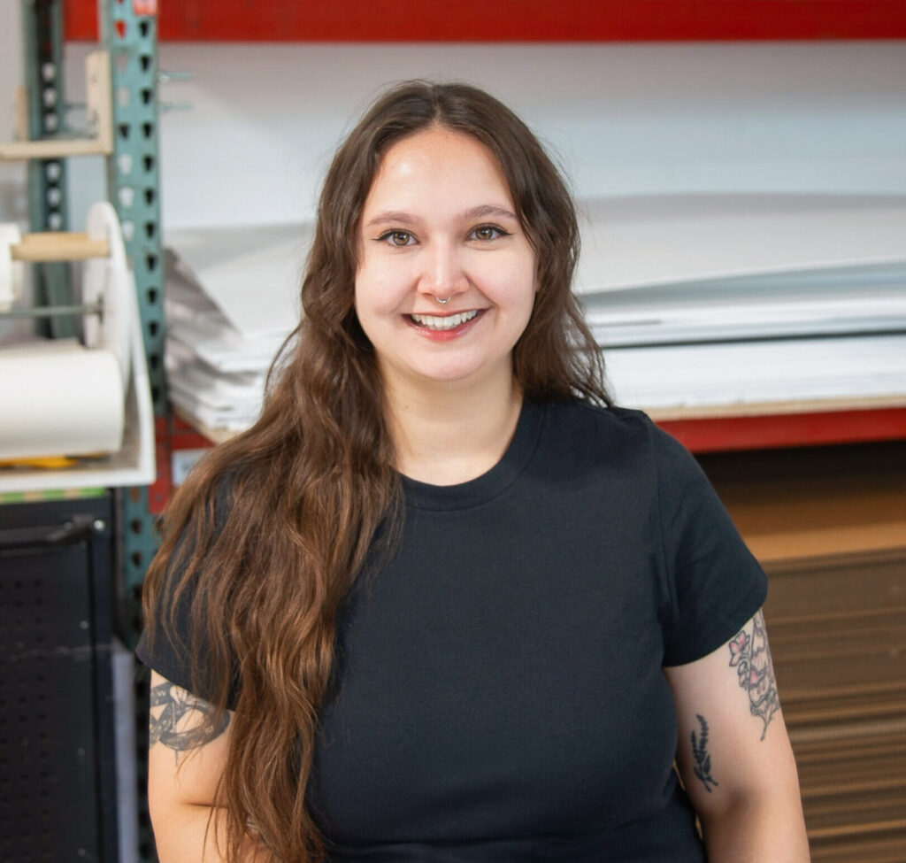 Kat Hasanov, Production Artist at HMR Designs, smiling in the workshop