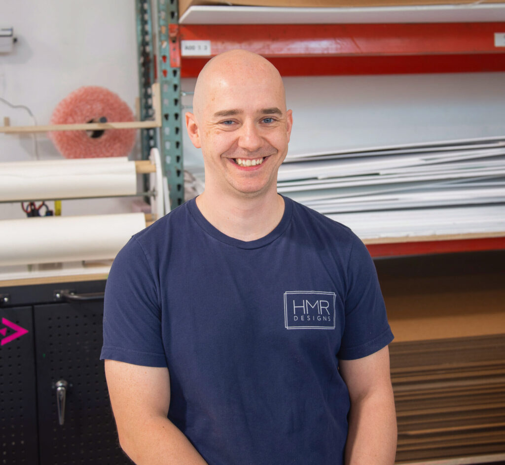Mariusz Szypulski, CNC Operator at HMR Designs, smiling in the workshop