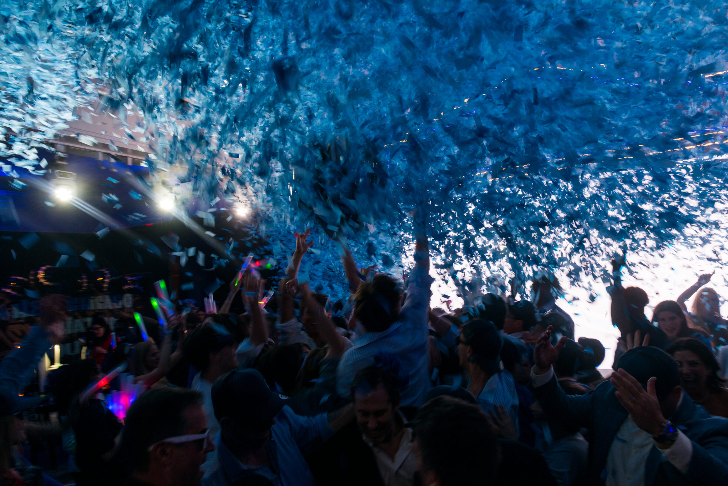 Guests dancing at a mitzvah celebration with blue confetti and dramatic event lighting