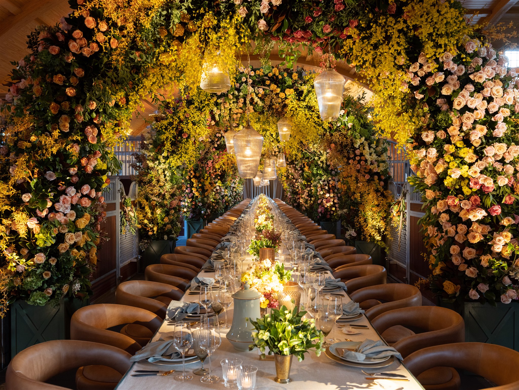 Long dinner table beneath lush overhead yellow florals and hanging lanterns by Rishi the Designer
